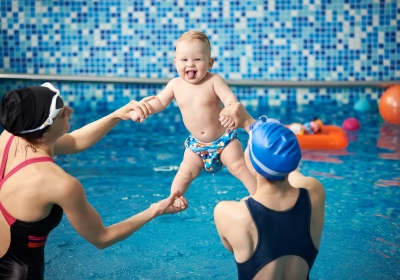 Women holding toddler lifting high up stretching exercising over water. Having fun in water. Activities in swimming pool